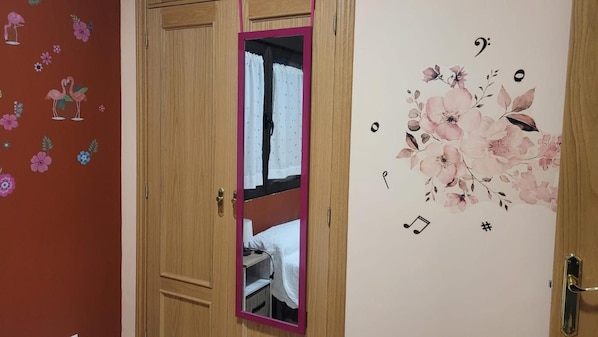 A room with a wooden door, a mirror, and a wall with floral and musical note decorations.