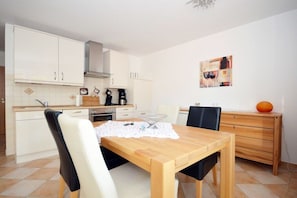 A compact kitchen with white cabinets, a wooden dining table, and a coffee machine. - Holiday apartment with 1 bedroom (Norddeich)