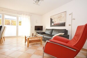 Un salon avec un canapé, un fauteuil rouge, une table basse et un téléviseur.