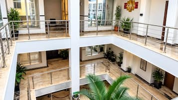 Un atrio de varios niveles con una columna central, barandillas de vidrio y plantas en macetas.