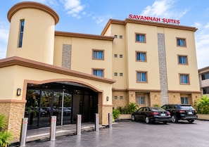 Um hotel com design moderno, apresentando uma entrada destacada com varanda coberta, várias janelas e uma placa com a inscrição 'SAVANNAH SUITES'.