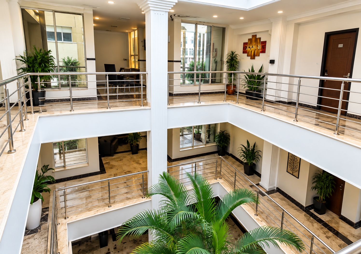 A multi-level interior with a central atrium, glass railings, and potted plants.
