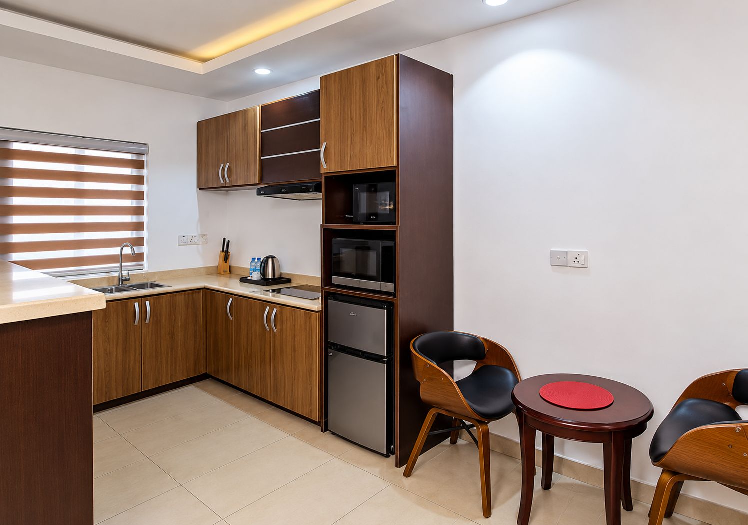 A modern kitchen with wooden cabinets, a built-in oven, and a dining area with two chairs and a small table.