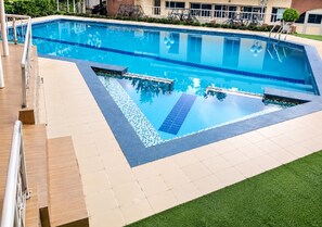Una piscina rectangular con borde de azulejos, rodeada por un solárium con baldosas y una zona de césped.