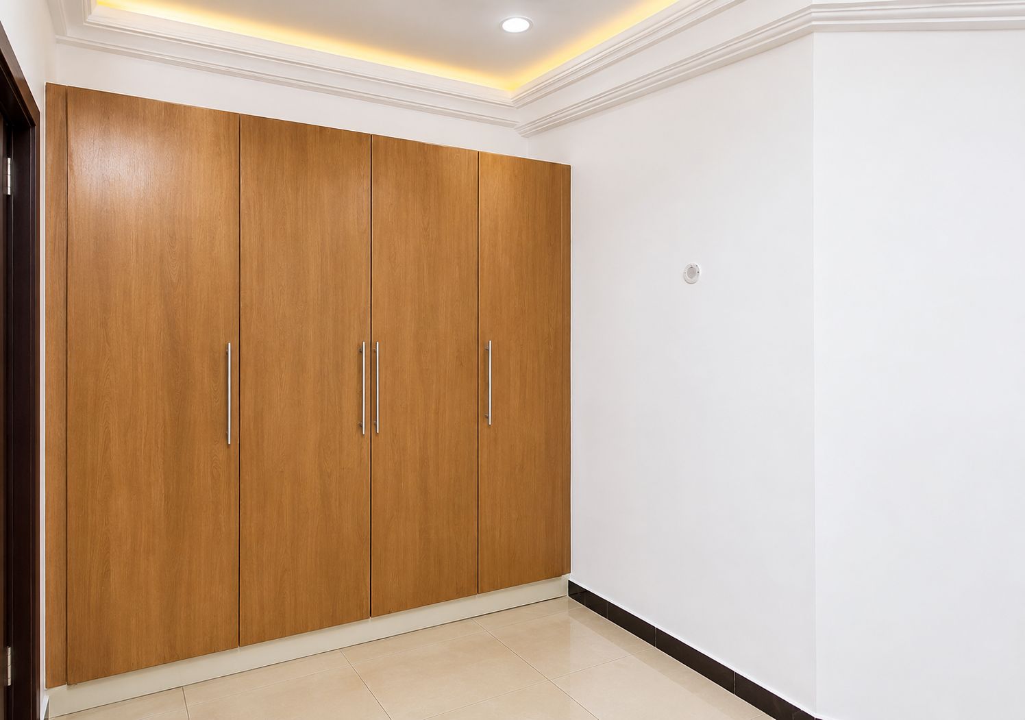 Quarto com um amplo guarda-roupa de madeira, piso ladrilhado e iluminação embutida no teto.