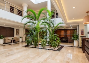 A spacious lobby with a high ceiling, a central plant arrangement, and a reception desk. - Savanna Suites & Hotel Garki Abuja (Abuja)
