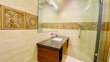 Un baño con pared de mármol, tocador de madera, cabina de ducha de vidrio y azulejos decorativos.