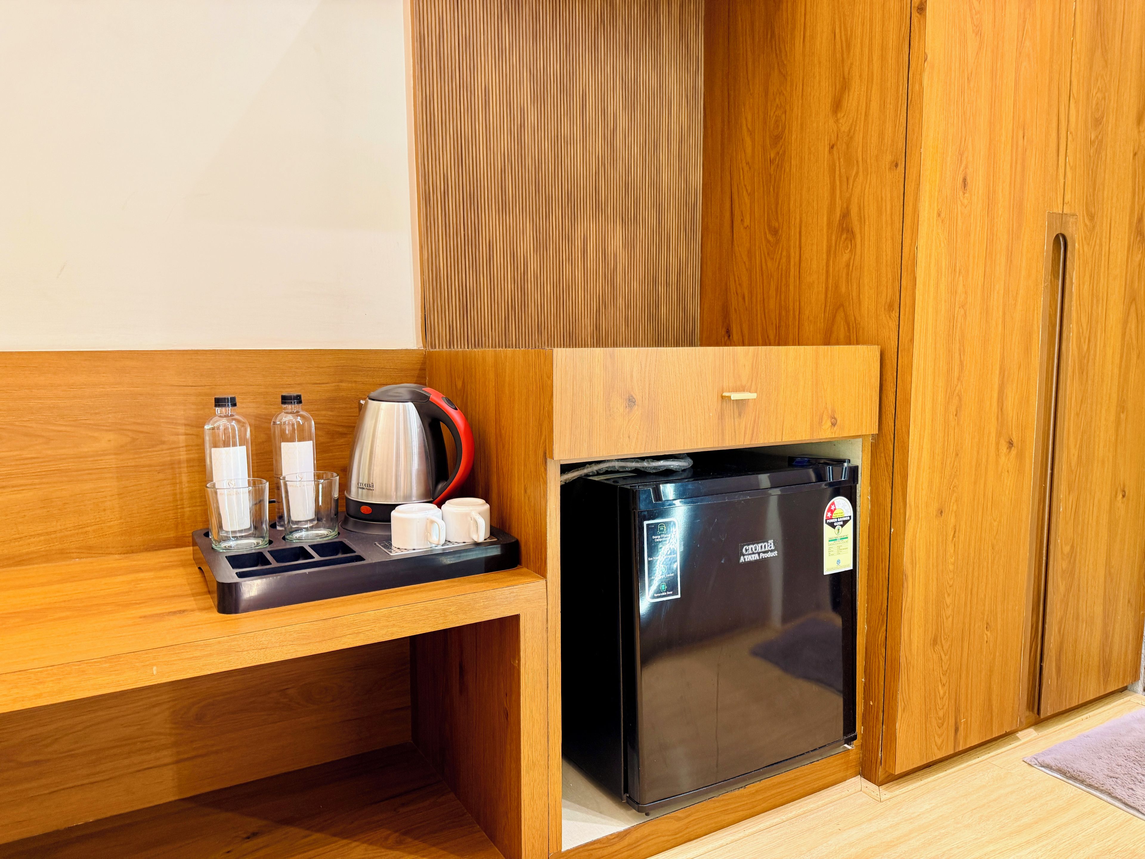 Una kitchenette compacta con un refrigerador negro, un hervidor y una cafetera.