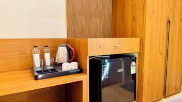 Una kitchenette compacta con un refrigerador negro, un hervidor y una cafetera.