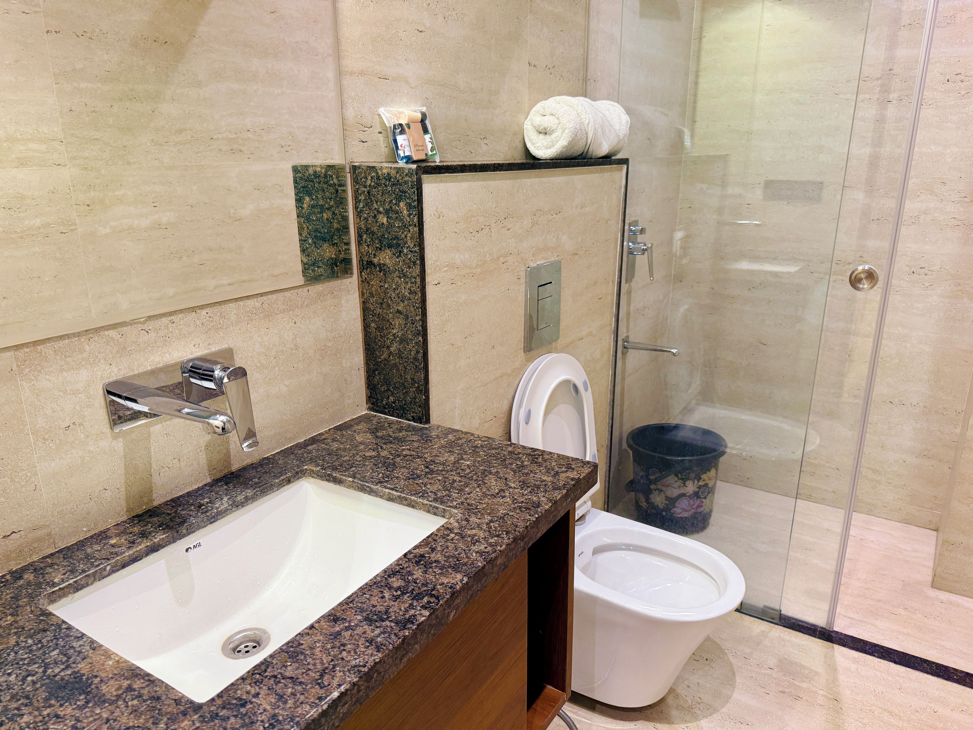 Un baño con lavamanos de encimera de granito, inodoro y zona de ducha.
