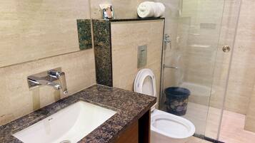Un baño con lavamanos de encimera de granito, inodoro y zona de ducha.
