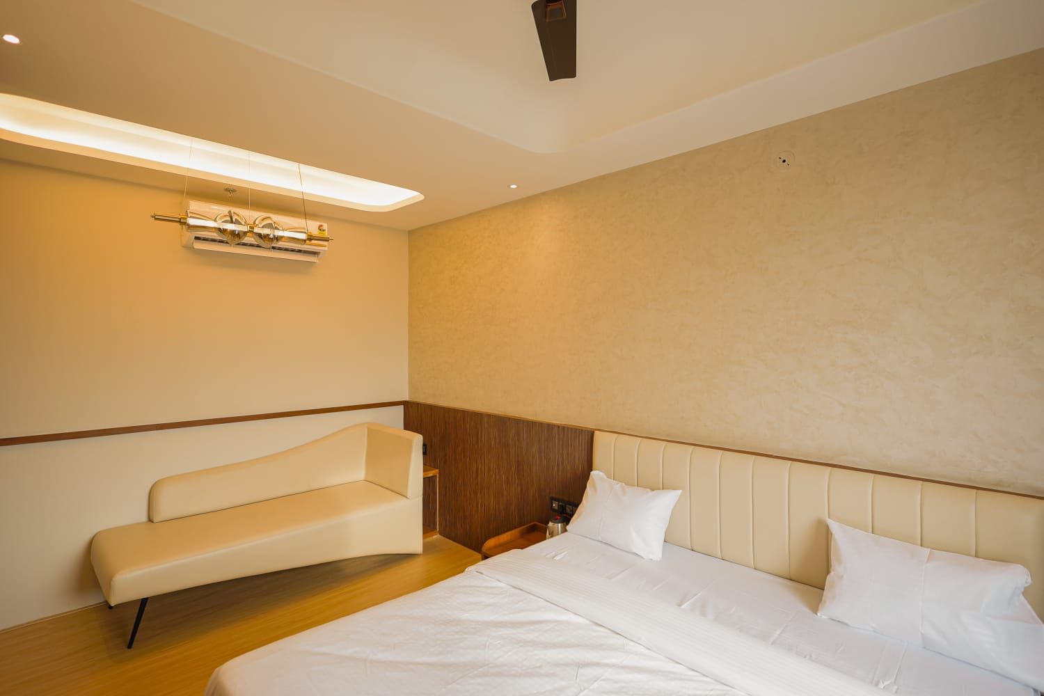 Una habitación de hotel con cama, un banco y un equipo de aire acondicionado instalado en la pared.