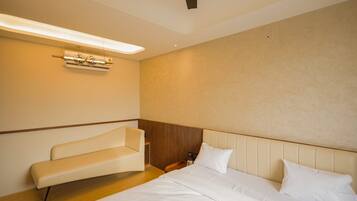 Una habitación de hotel con cama, un banco y un equipo de aire acondicionado instalado en la pared.