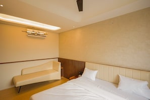A hotel room with a bed, a bench, and a wall-mounted air conditioning unit. - Golden Sands Hotel And Banquets (Indore)