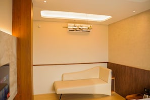 A modern hotel room with a sofa, a ceiling light fixture, and a wooden accent wall. - Golden Sands Hotel And Banquets (Indore)