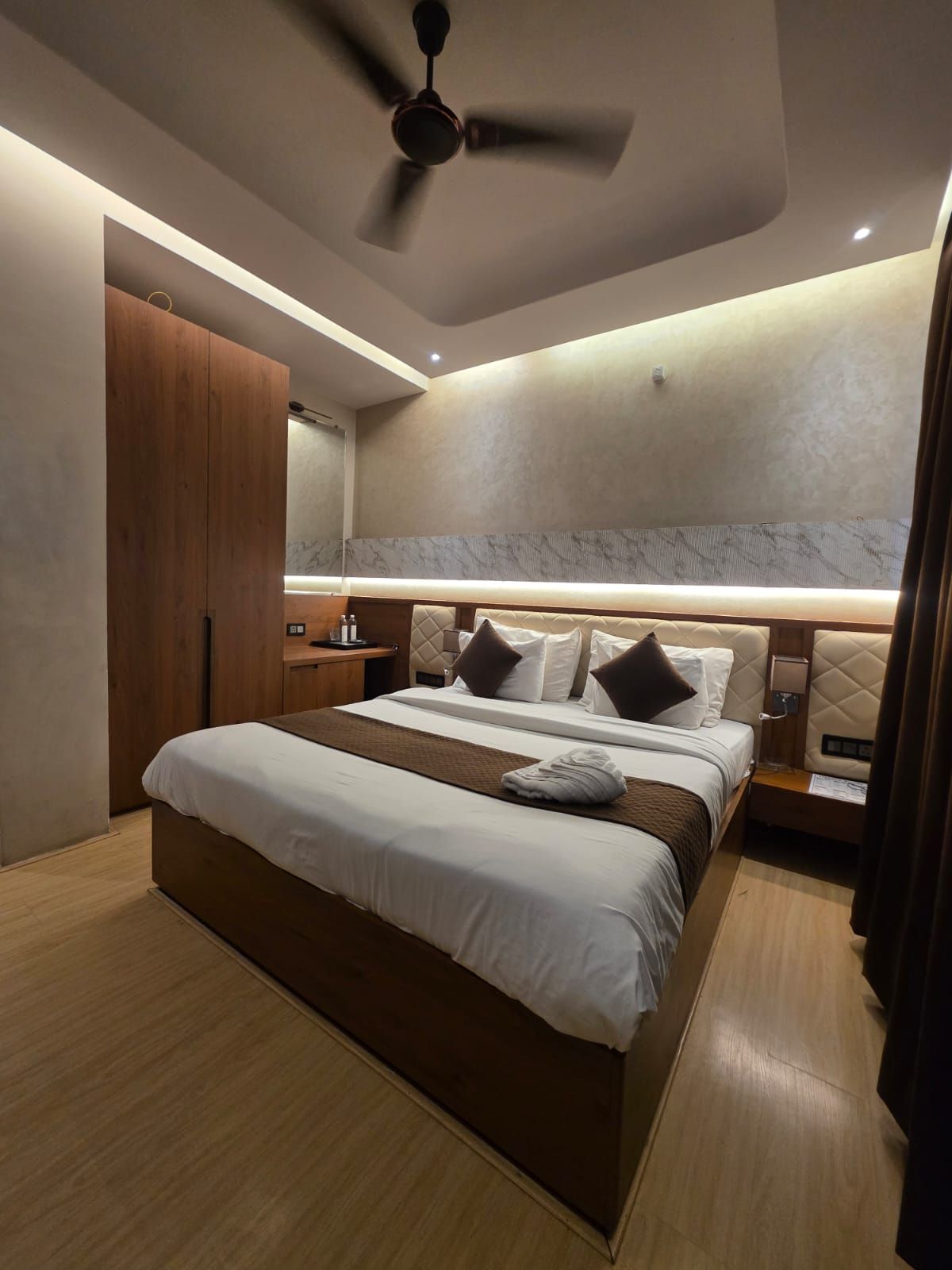 Una habitación de hotel moderna con una cama grande, un ventilador de techo y una pared de acento de mármol.