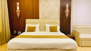 A hotel room with a large bed, two bedside tables, a bedside lamp, and a chair. - Golden Sands Hotel And Banquets (Indore)