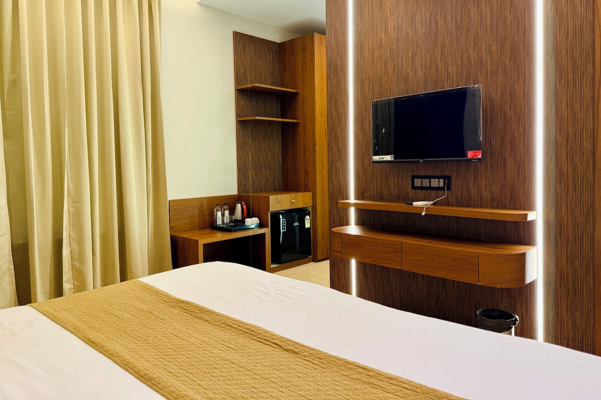 A hotel room with a bed, a television mounted on the wall, a coffee machine, and a small desk area.