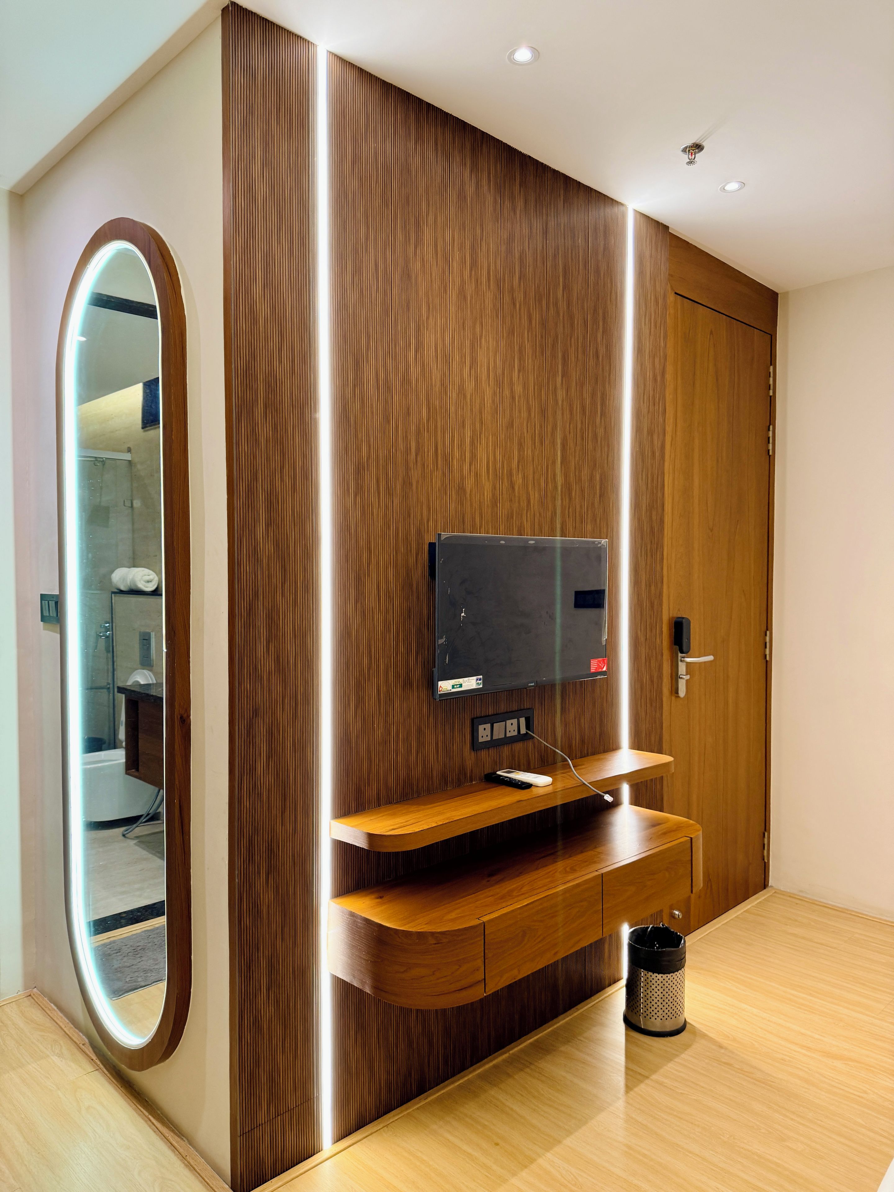 Una habitación moderna con un panel de madera en la pared, televisor integrado y un espejo.