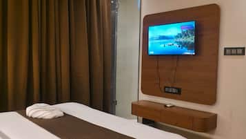 Una habitación de hotel con una cama, un televisor montado en la pared, un equipo de aire acondicionado y un ventanal con cortinas.