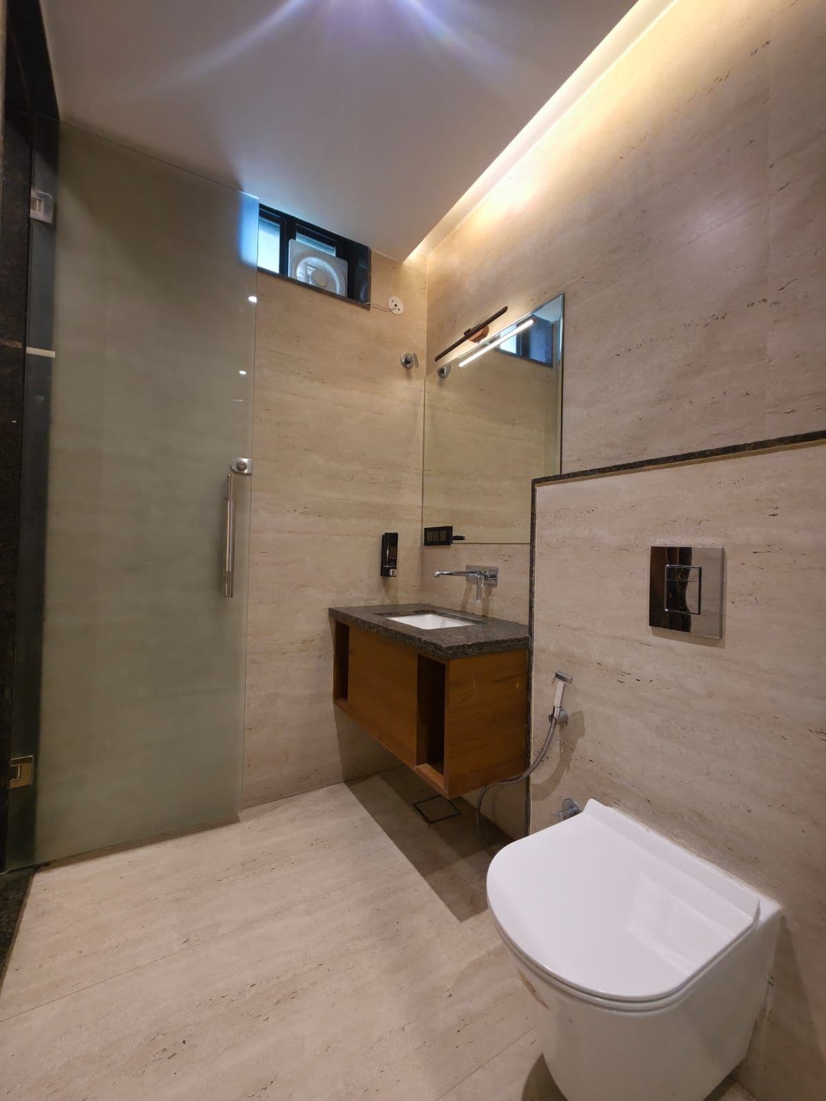 Un baño moderno con cabina de ducha de vidrio, tocador de madera y un inodoro blanco.