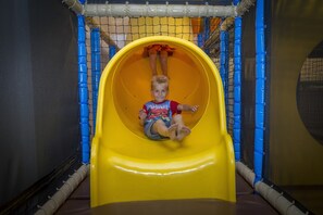 A child on a yellow slide inside a play area with netted walls.
