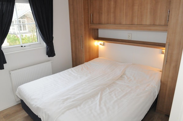 A single bed with white bedding in a room with a window, a radiator, and wooden furniture.