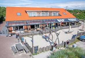 Un restaurant avec un toit recouvert de tuiles rouges, des tables en plein air et une clôture en bois.