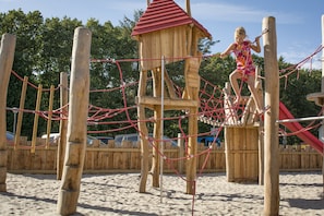 A wooden play structure with a rope net and a small red-roofed tower.