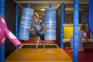 Un enfant joue dans un espace de jeux sécurisé, avec des murs bleus et jaunes et un sol orange doux.