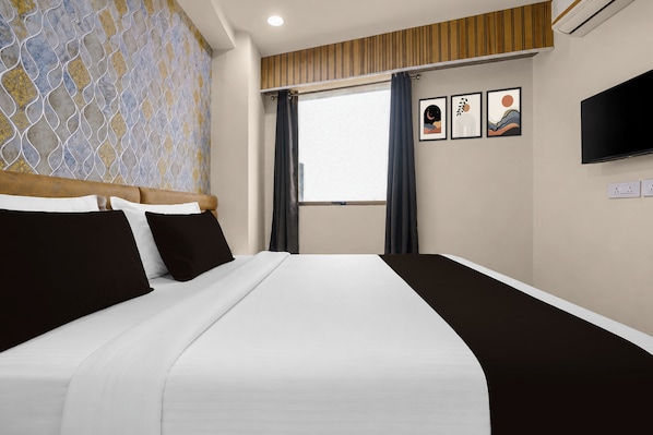Quarto de hotel com cama, televisão, janela com cortinas e papel de parede estampado.