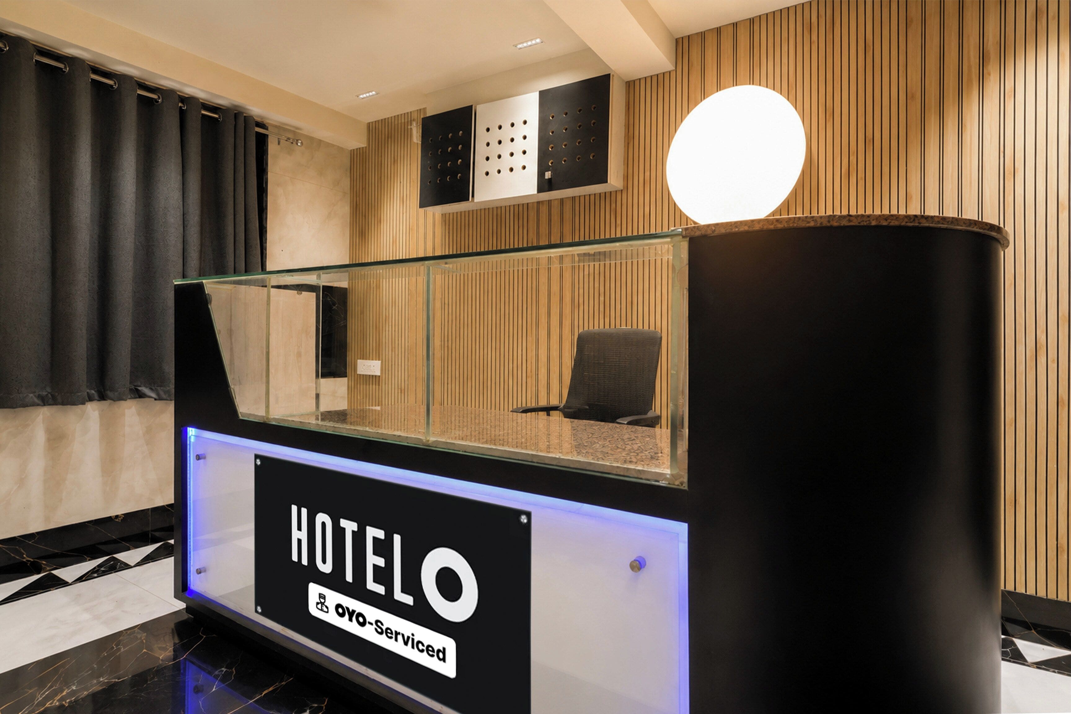 A hotel reception desk with a glass partition, a black sign reading 'HOTELO', and a wooden wall with vertical slats.