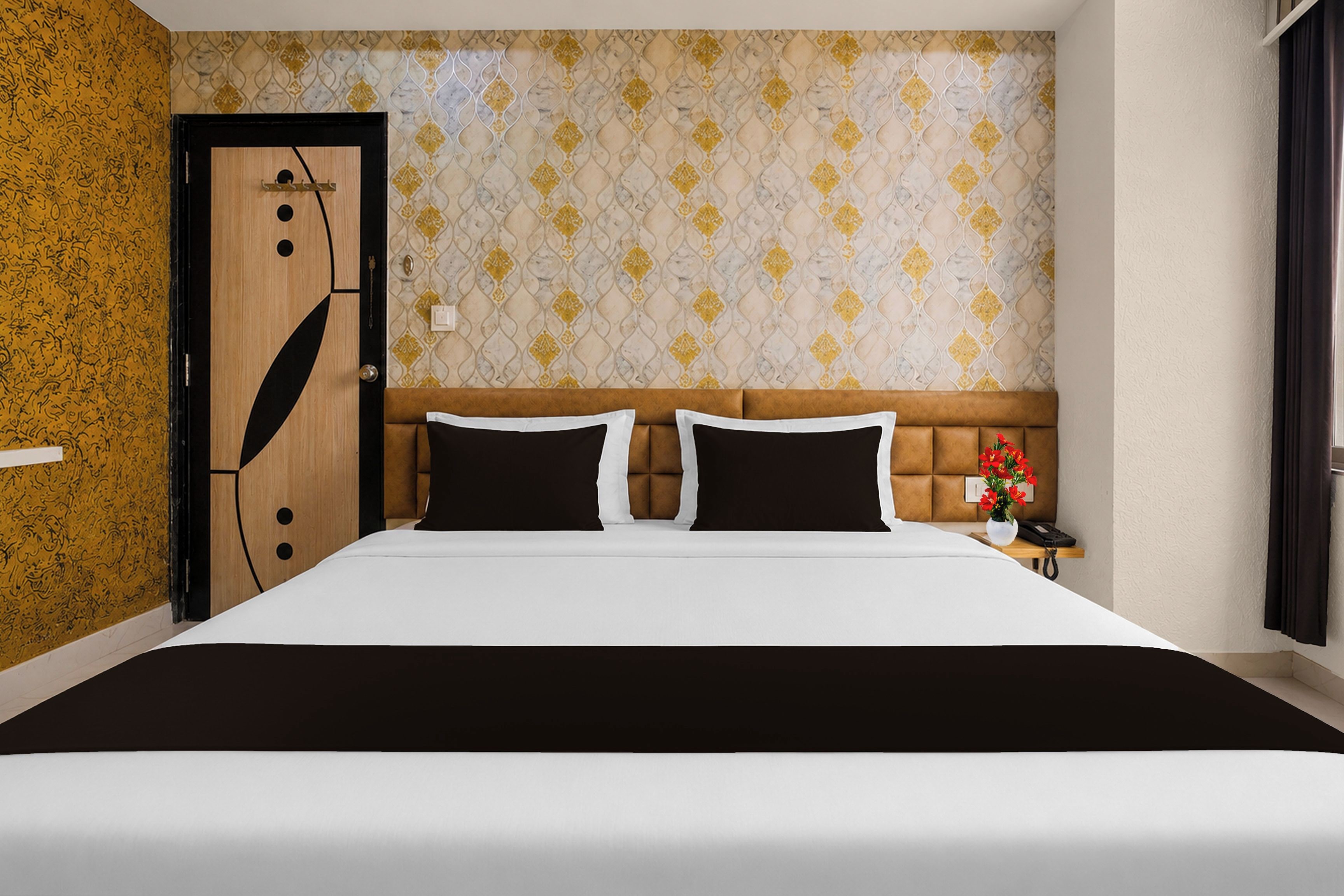 Une chambre d’hôtel avec un grand lit, une porte en bois, un papier peint à motifs et une table de chevet ornée d’un vase de fleurs.