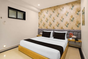 Habitación de hotel con cama, mesita de noche, teléfono y un panel decorativo en la pared.