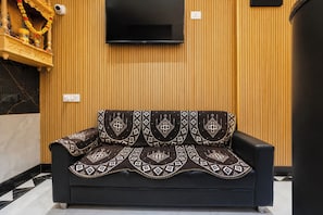 Un sofá negro con cojines estampados frente a una pared de madera con un televisor de pantalla plana montado en la parte superior.