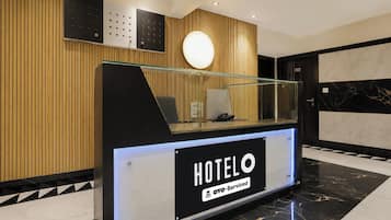 Un comptoir d’accueil d’hôtel avec une cloison en verre, un téléphone et un panneau indiquant que l’établissement est géré par OYO.