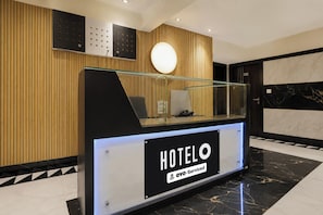 Un mostrador de recepción de hotel con un separador de vidrio, un teléfono y un cartel que indica que es atendido por OYO.