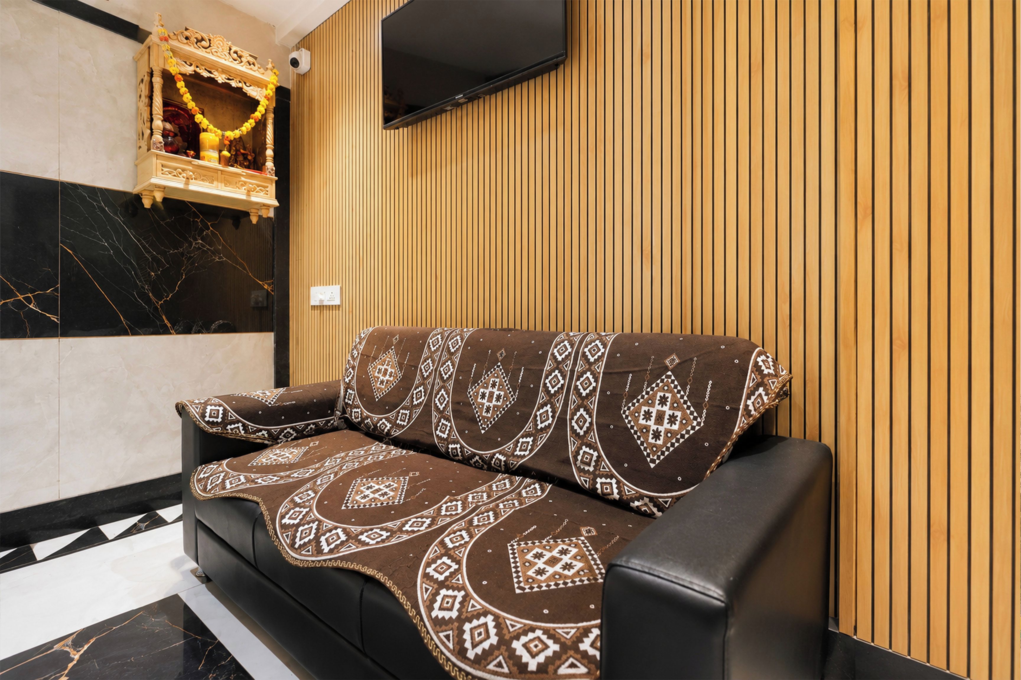 A modern living room with a black leather sofa, patterned throw, and a wooden wall panel.