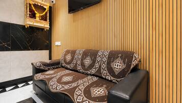 A modern living room with a black leather sofa, patterned throw, and a wooden wall panel.