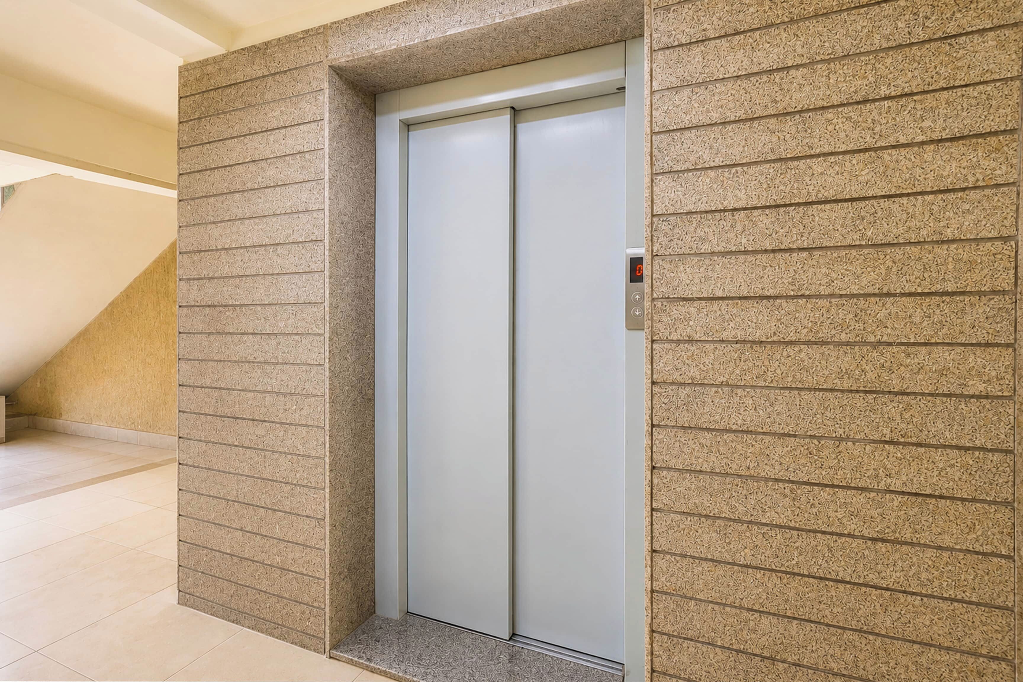 Un ascenseur moderne doté d’un écran numérique, installé dans un couloir aux murs texturés et au plafond incliné.