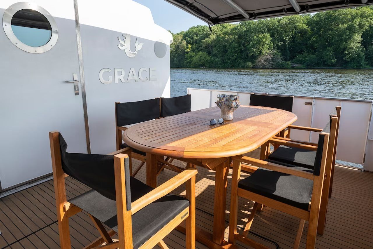 A wooden deck with a table and chairs, a potted plant, and a view of a river.