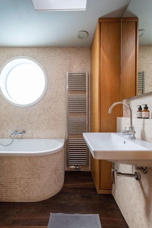 A modern bathroom with a freestanding bathtub, a round mirror, and a built-in sink. - Schiff Grace (Berlin)