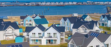 A coastal residential area with houses featuring balconies and solar panels, a pier extending into the water, and a clear view of the sea.