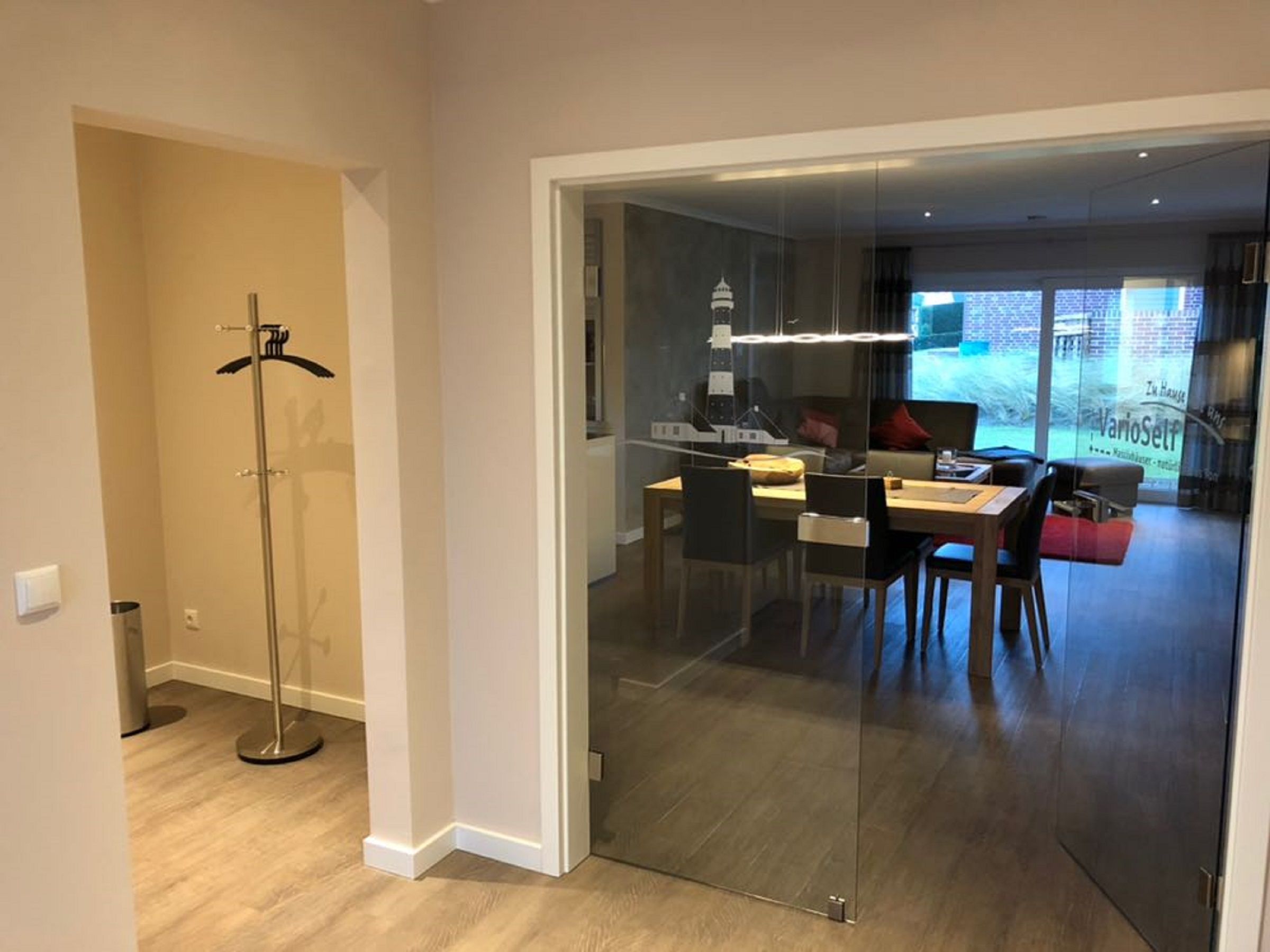 A modern interior with a dining area, a coat rack, and a view through a glass door.