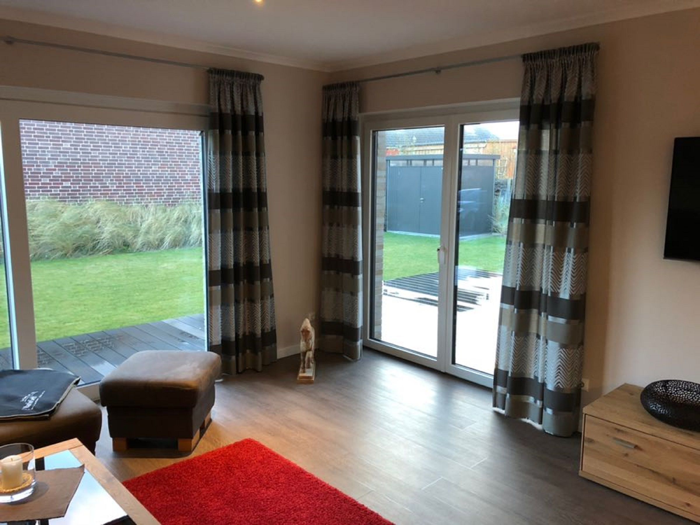 A spacious living room with a large sliding glass door leading to a backyard, a comfortable seating area with a red rug, and a wooden floor.