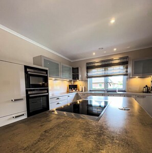 A modern kitchen with a central island, built-in appliances, and a window providing natural light. - "Winkelbungalow" Holiday Home in Garding: Spacious living with the utmost comfor (Garding)