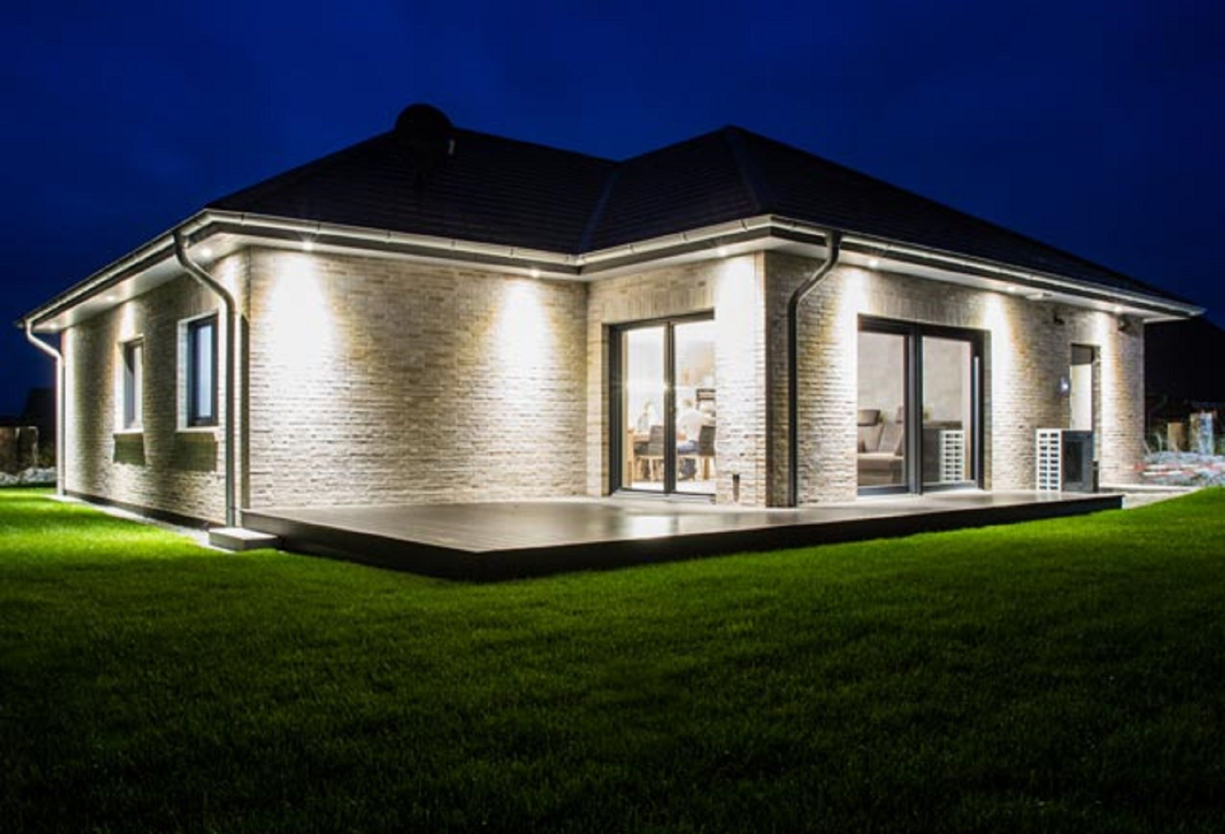A modern house with a brick exterior, large windows, and a well-lit patio area.