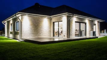 A modern house with a brick exterior, large windows, and a well-lit patio area.