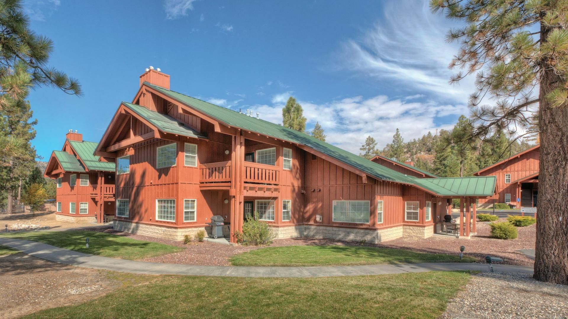 A large, multi-story wooden house with a green roof, surrounded by a well-maintained lawn and trees.