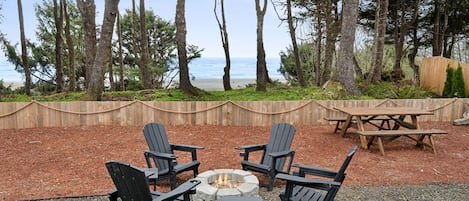 An outdoor seating area with Adirondack chairs and a fire pit, surrounded by a wooden deck and a view of the ocean.